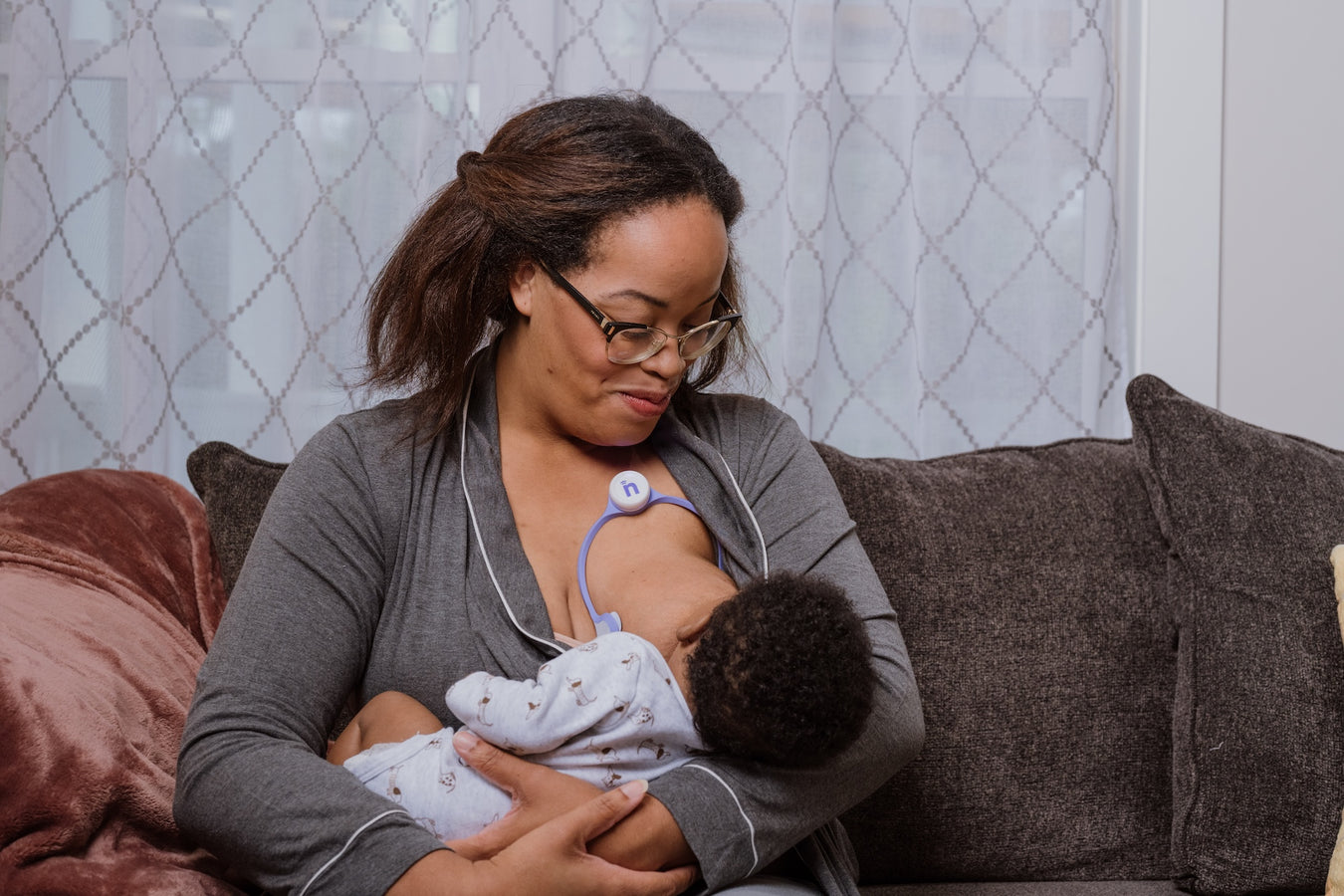 Woman breastfeeding a baby on a couch with a neutral background