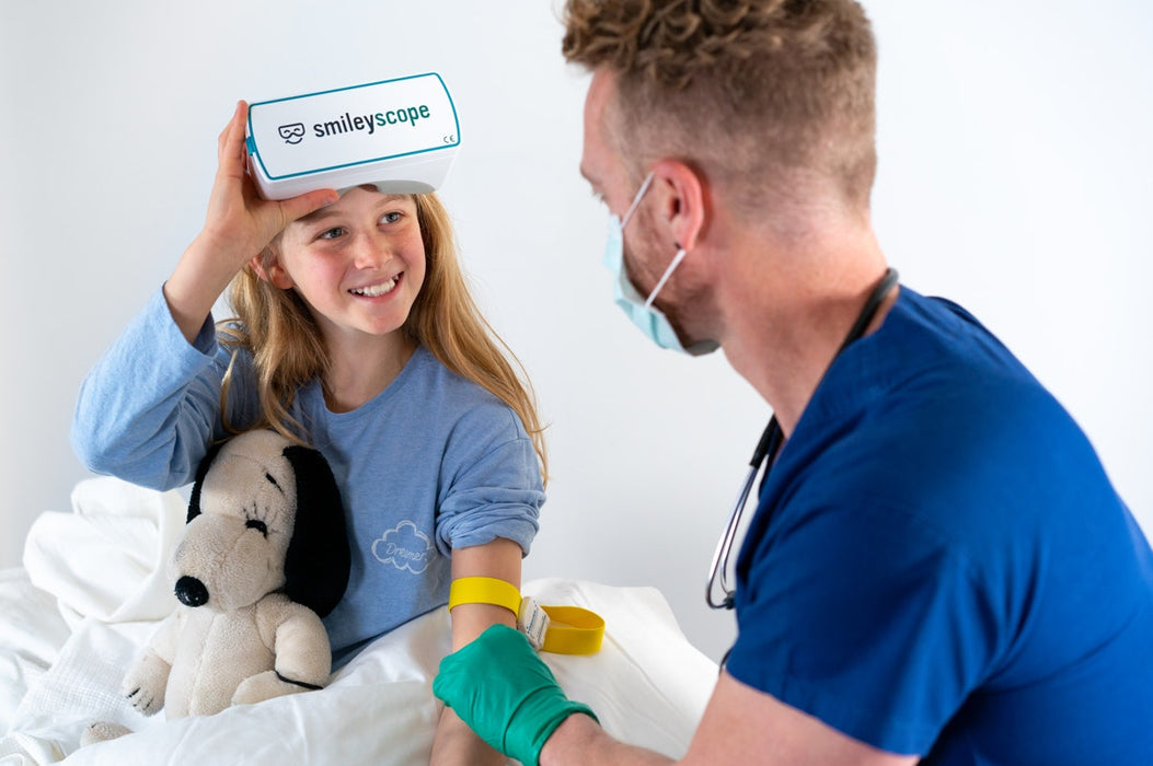 Child holding a 'smileyscope' device with a doctor examining them, both wearing blue scrubs.