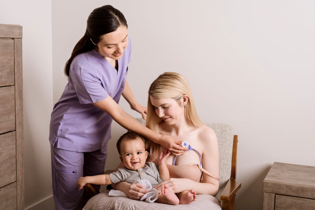 Woman breastfeeding a baby with a healthcare professional assisting in a home setting.