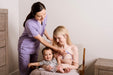 Woman breastfeeding a baby with a healthcare professional assisting in a home setting.
